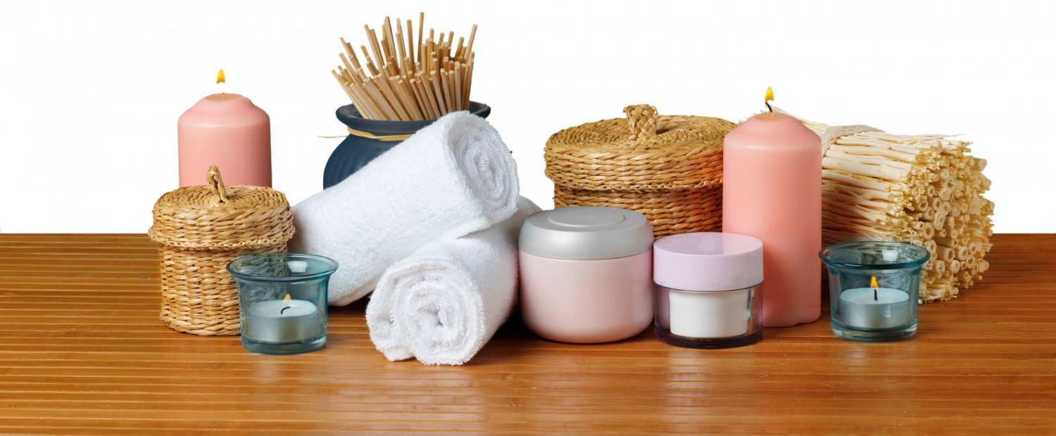 Serviettes blanches roulées, produits de soin et bougies posés sur un plan de travail en bois